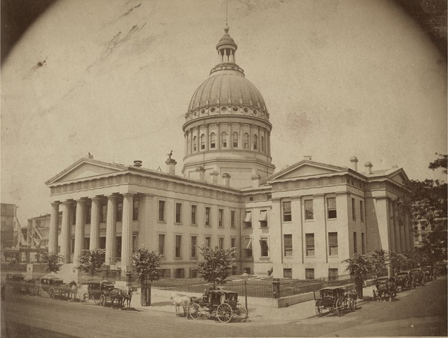 Black and white photo of a large courthouse building with copper domed roof and four square wings.
