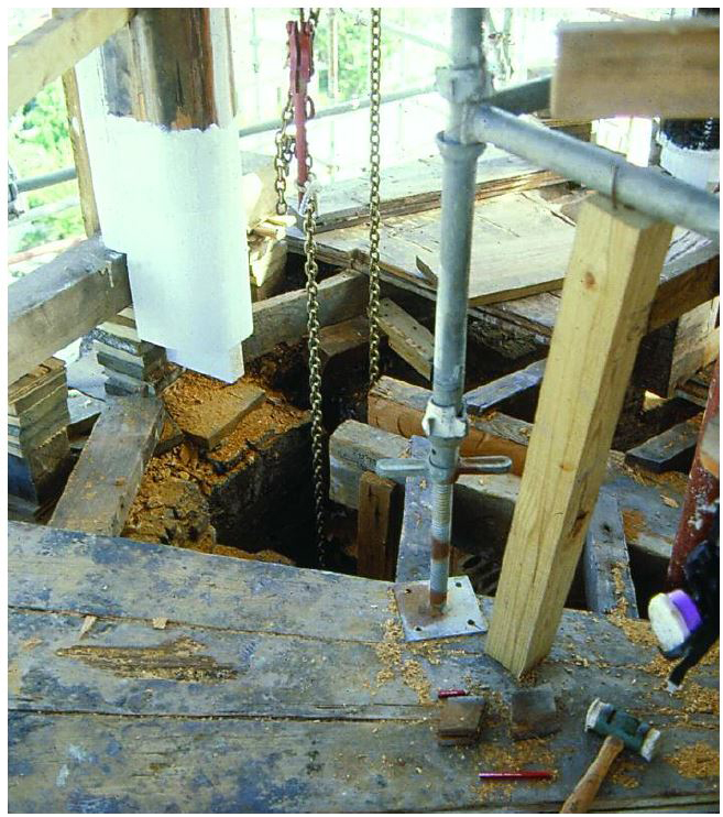 A new post with exposed tenon joint rising out of a weathered deck with missing boards.