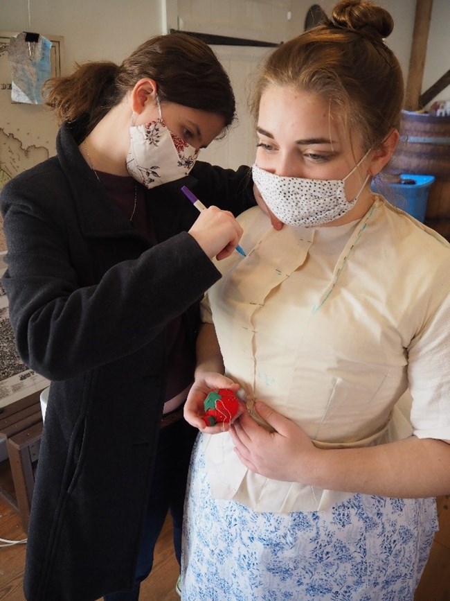 A woman fits another woman for a Victorian dress.