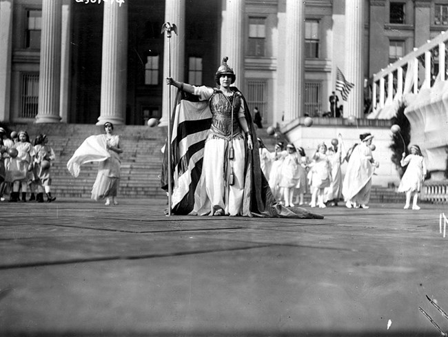 a woman dressed as mythical Columbia poses in front of the treasury building LOC