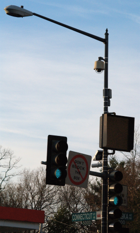 A surveillance camera mounted on a stop-light at an intersection.