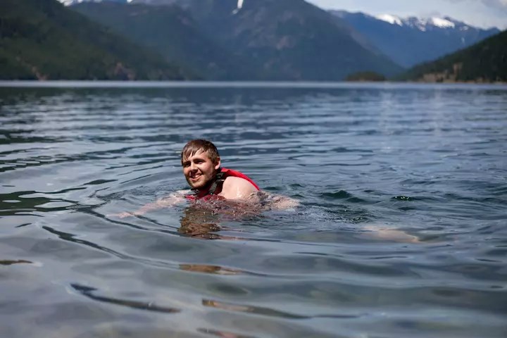 A man swimming in a lake surrounded by tall mountains