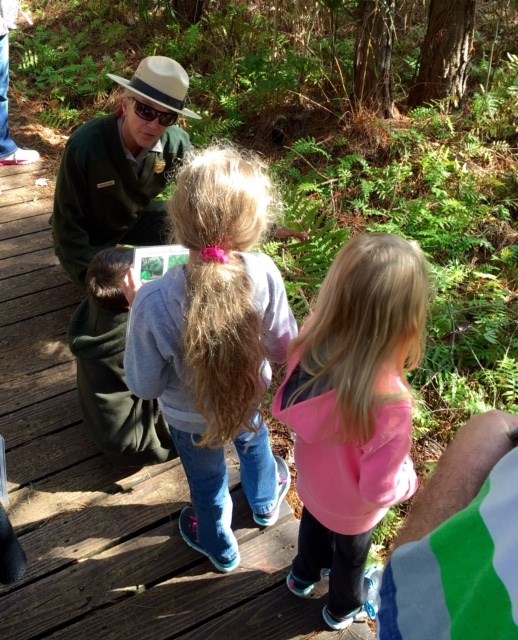 A ranger crouches to speak to two children.