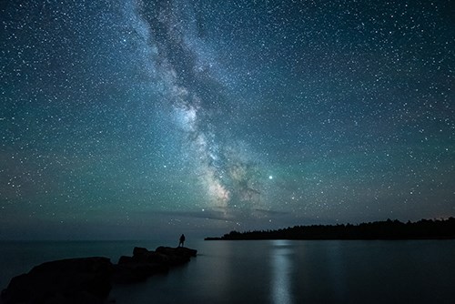 Dark sky with Milky Way, reflected in water with dark landforms.