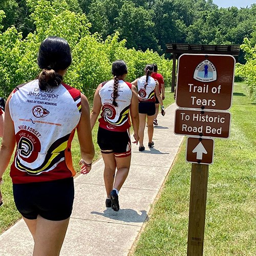People walking on cement path next to trail sign.