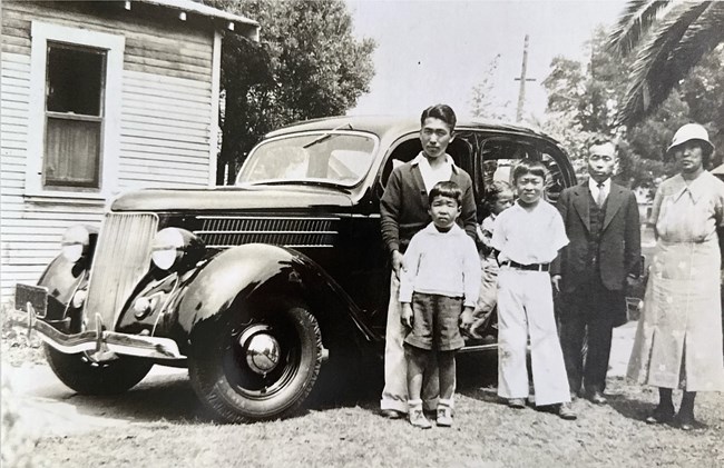 Black and white photo of a family of six standing in front of a 1930s car