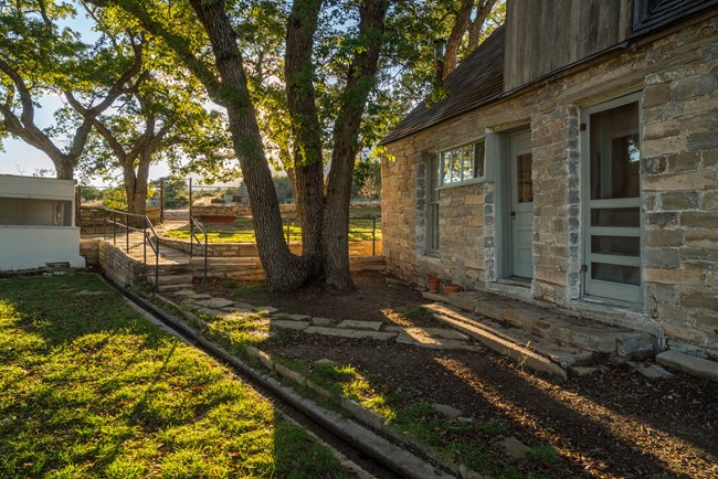 A stone house is fronted by a yard with a small channel of water flowing through it