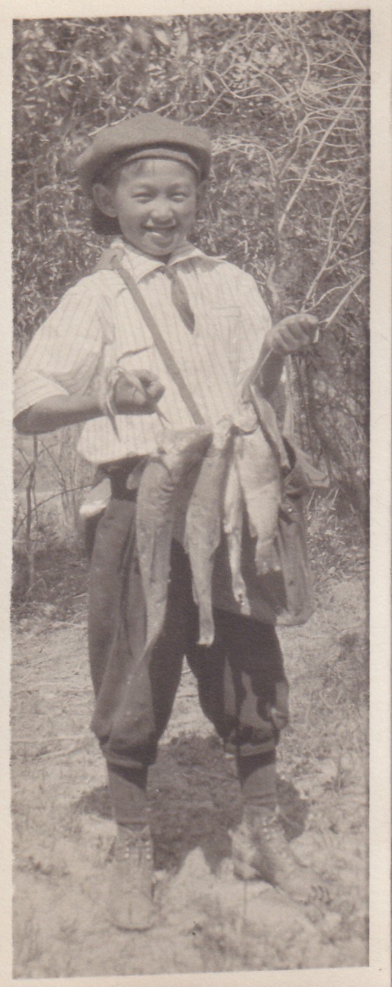 A young Japanese American boy smiling while holding up a string of fish