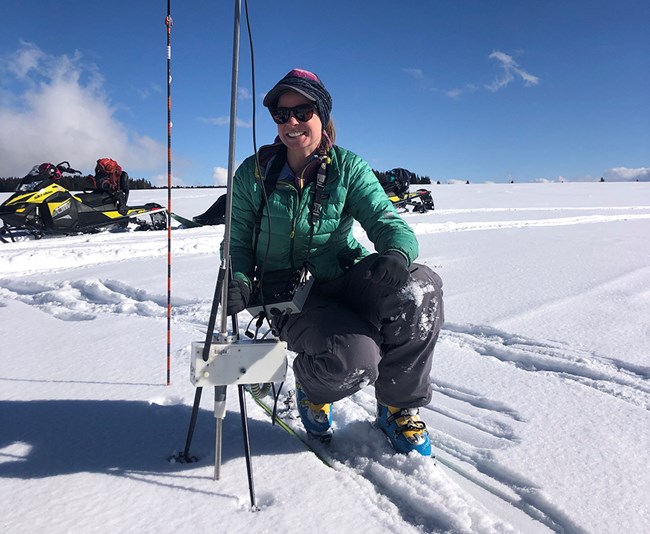 Snow scientist on skis squatting low to measure snow layer hardness with digital equipment.