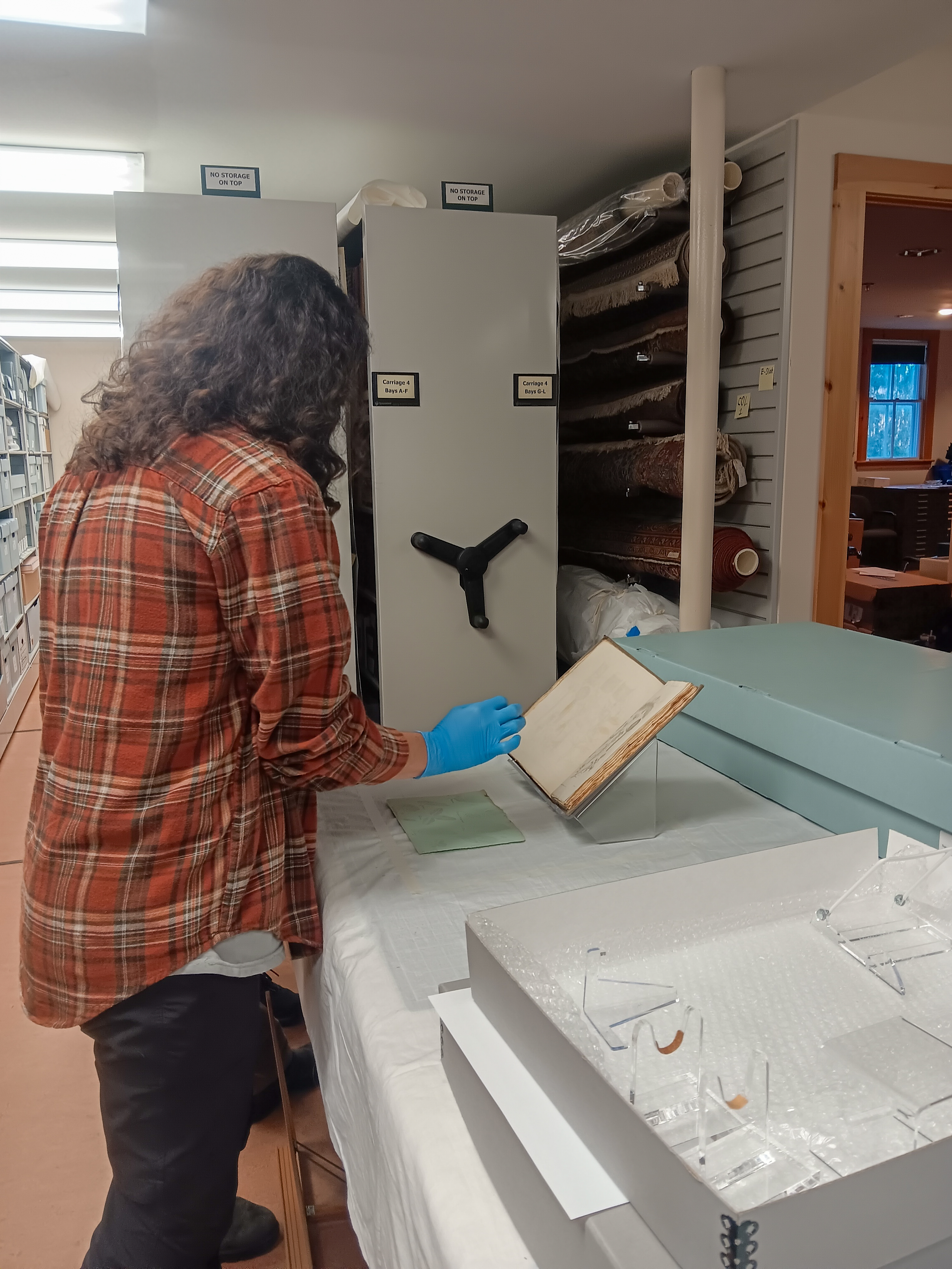 person wearing blue curatorial gloves carefully examines a historical book in the park archives