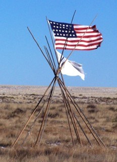 A tipi frame at Sand Creek Massacre site with American and white flag of surrender beside it