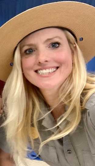 A close-up image of a blonde woman in a tan round hat smiling.