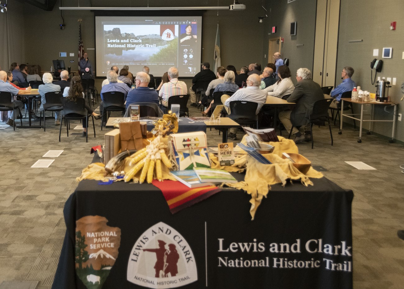 A table covered in items relating to Lewis and Clark with people in the background
