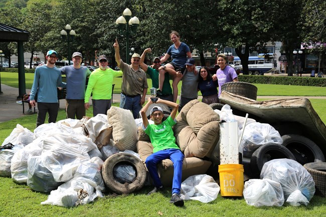 A group stands among a large pile of debris smiling and celebrating, one sits among the debris holding a trophy.
