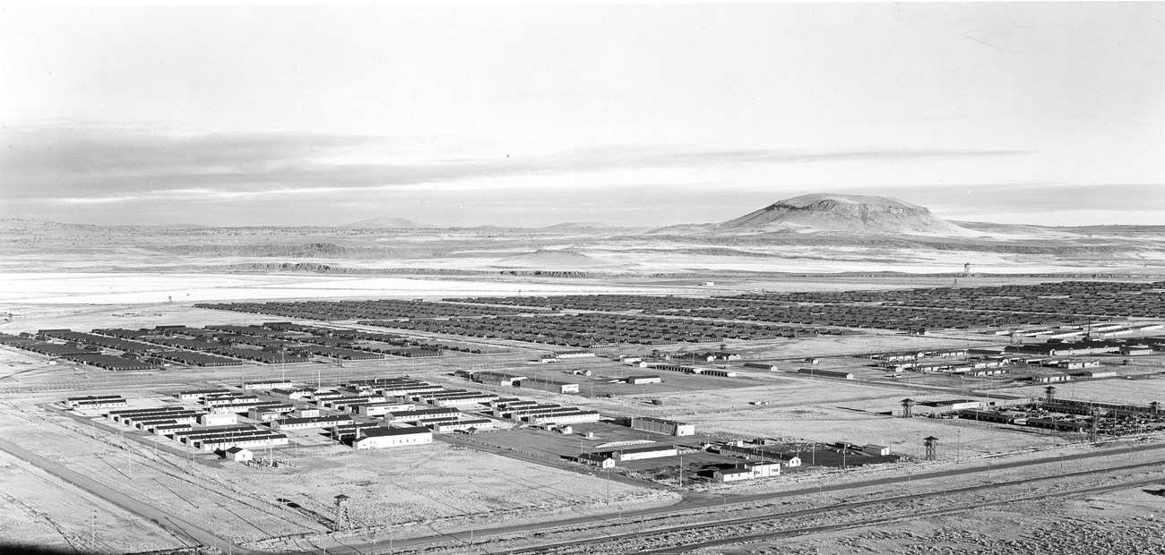 Historic black and white photo of a large camp complex in a high desert