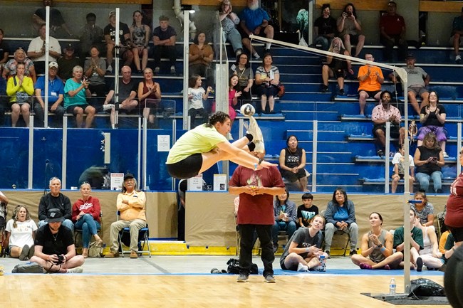 a young woman folds her body in half mid-air to kick a suspended ball with two feet.