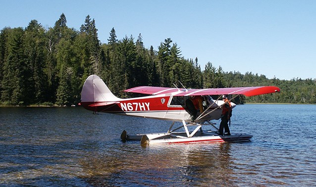 A red and white float plane on shallow water with forest in the background
