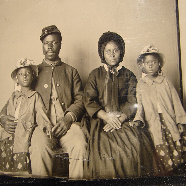 An African American solider in Union Army uniform seated with his family