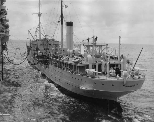 Black and white image of a ship on the water with fuel tubes extending from its side