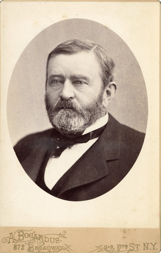 Black and white photo of bearded man wearing a suit and bow tie.