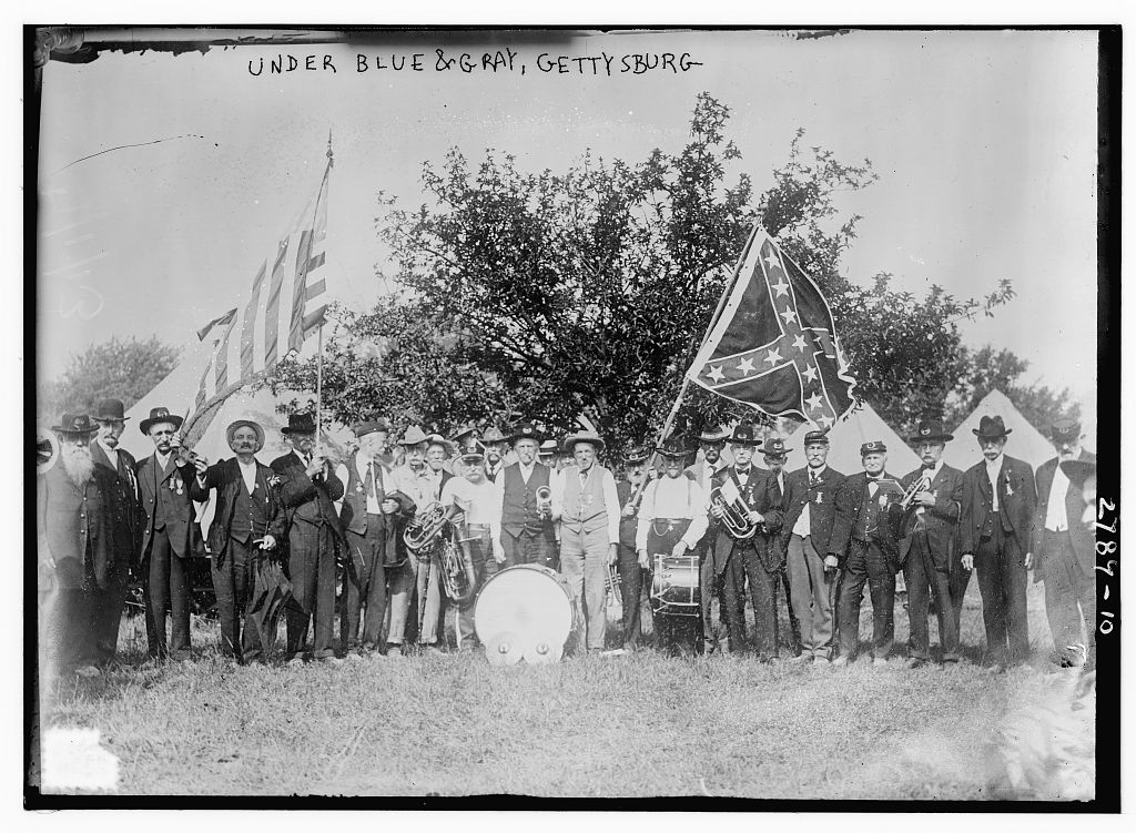 White men standing with two large flags: the U.S. flag and the battle flag of the Confederacy
