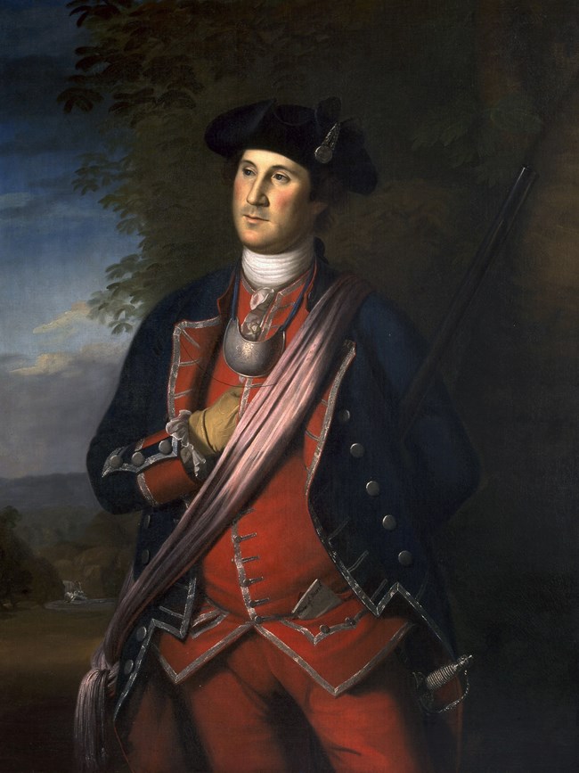 Man standing, wearing a red militia uniform with a blue coat and black tri-corner hat.