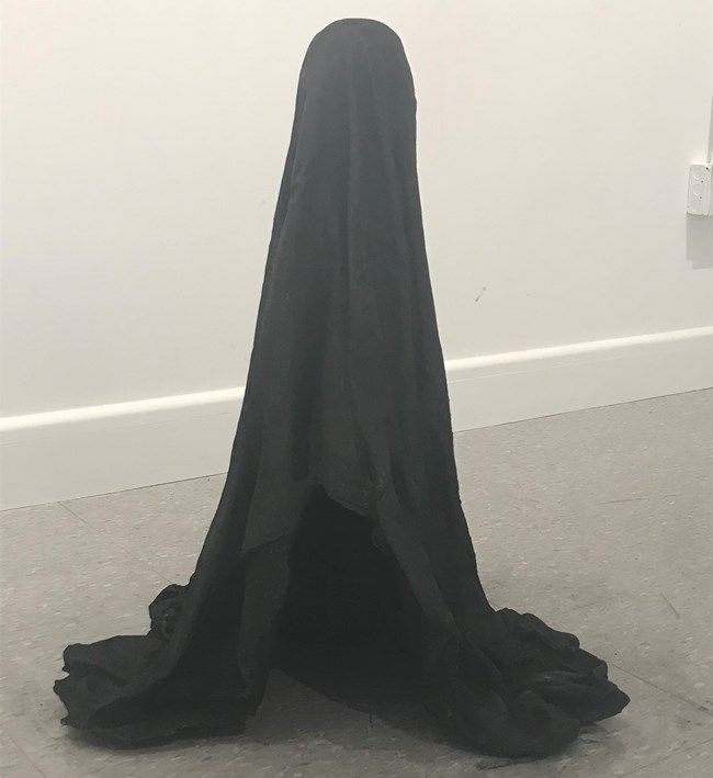 Cast iron depiction of a bedsheet draped over someone or something giving the illusion of a ghost