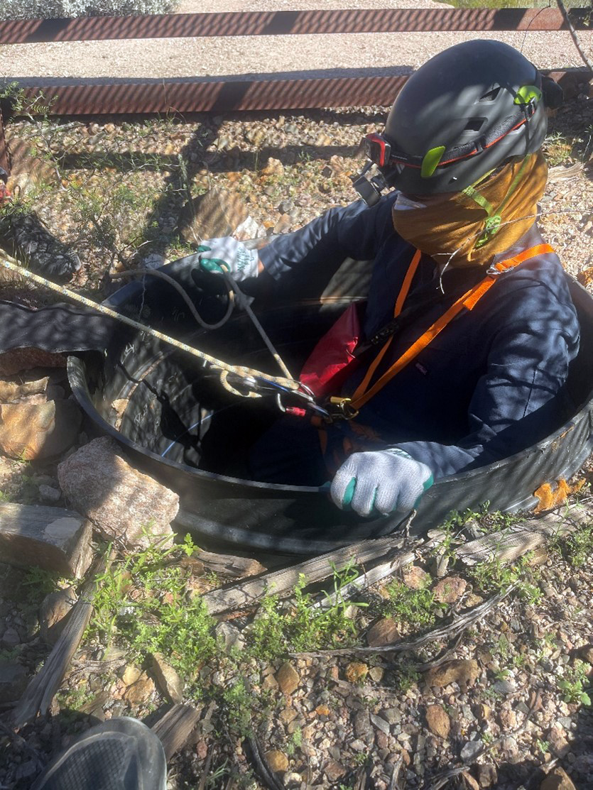 a person in climbing gear repeals into a small culvert in the ground