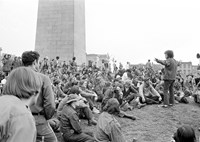 group of people sitting in front of the Bunker Hill Monument. One person is standing and speaking to the group.