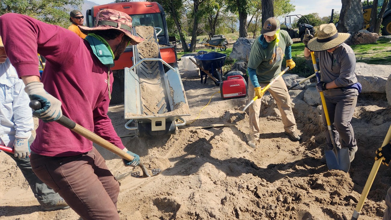 Group of people shoveling sand onto conveyor belt