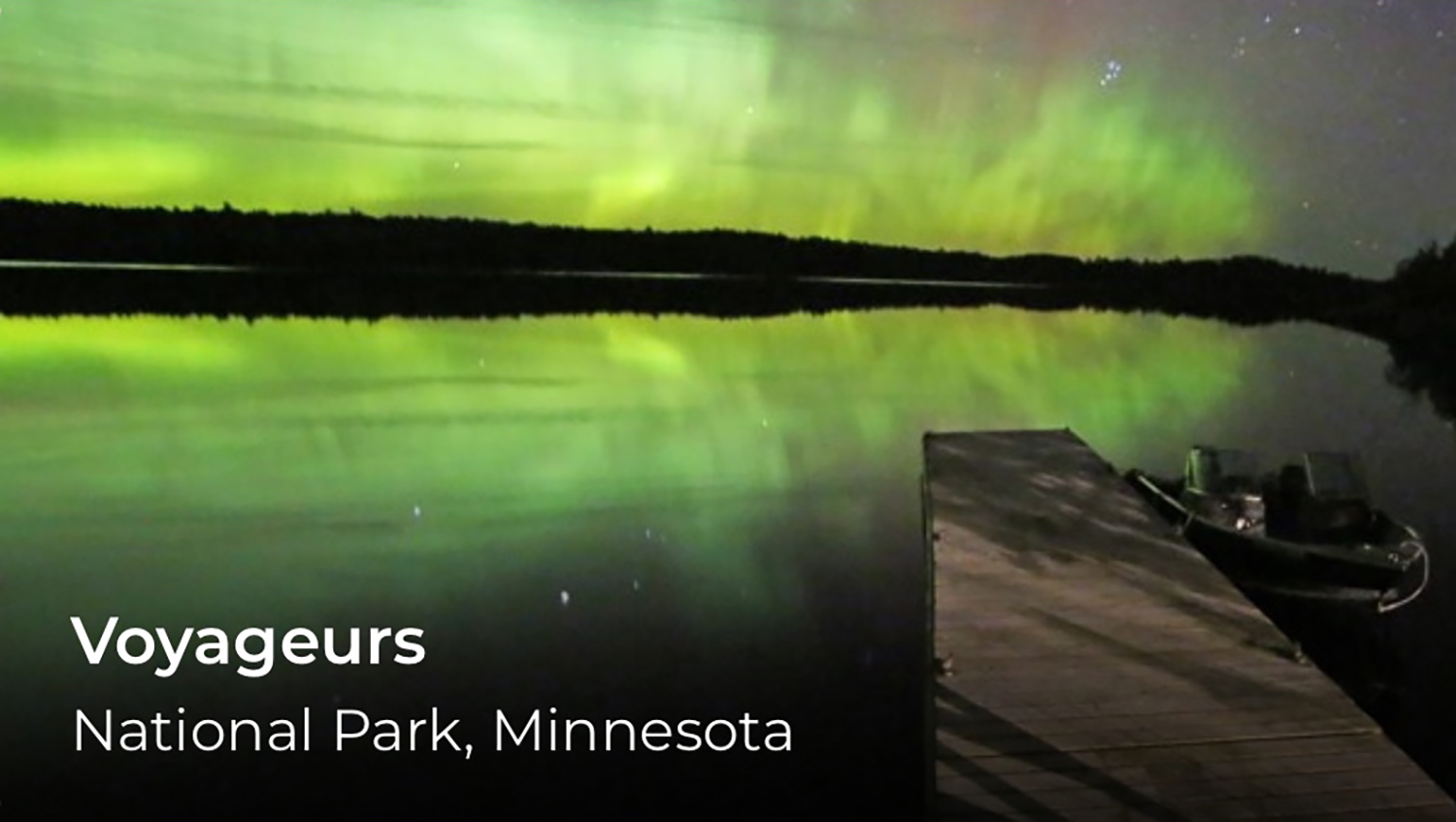 The aurora borealis over the water. Voyageurs is written in the lower left.