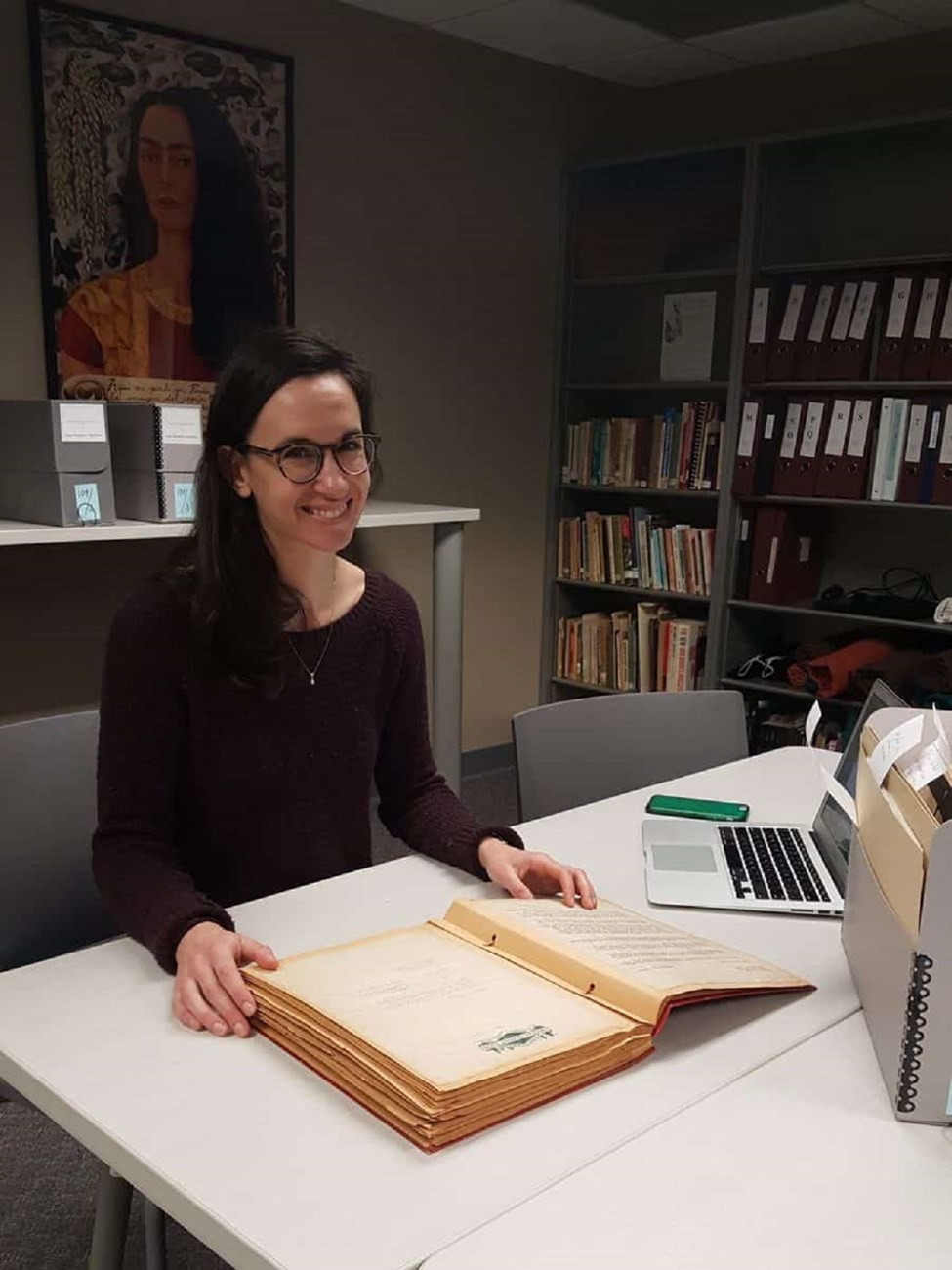 Ella conducting archival research in the Iowa Women’s Archives sitting in a desk with a very large book.