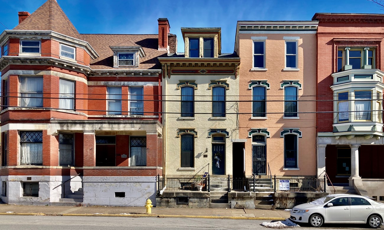 Historic nineteenth century brick buildings in various colors and detailed facades line bright city street