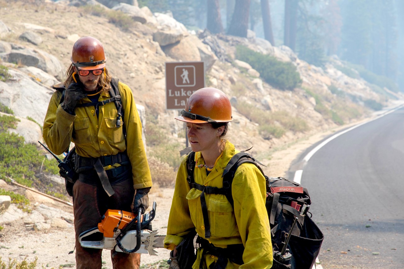 Wildland firefighters walking along a road through thick haze.