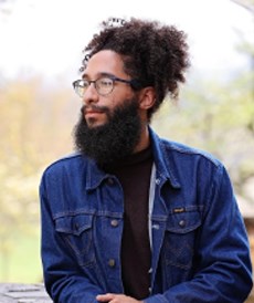 a bearded black man wearing glasses and a bun in his hair