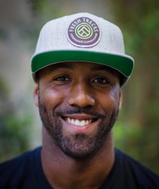 a black man smiling wearing a green and gray cap