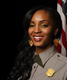 a black woman wearing a park ranger uniform in front of an American flag
