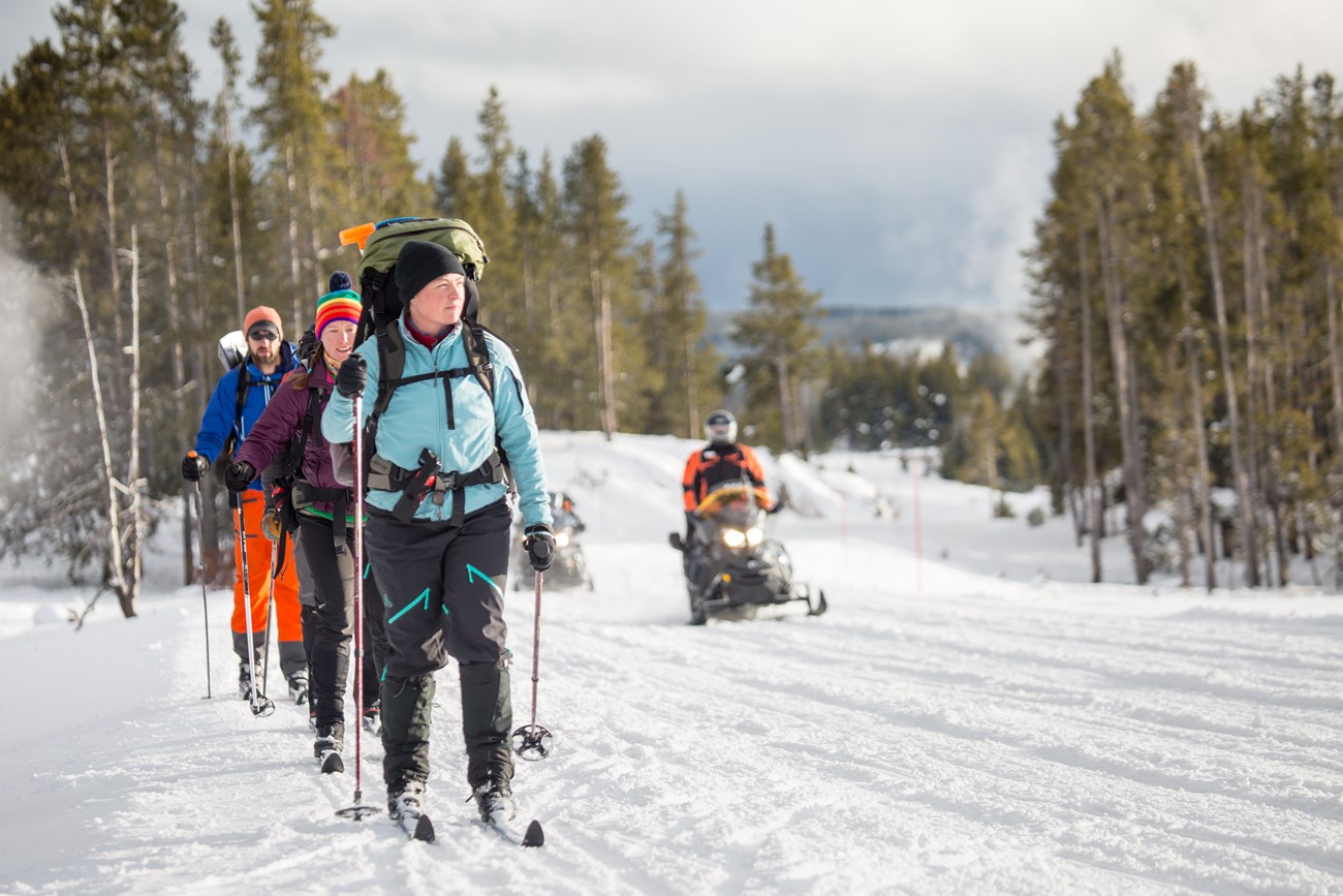 a snowmobile passes a line of winter skiers