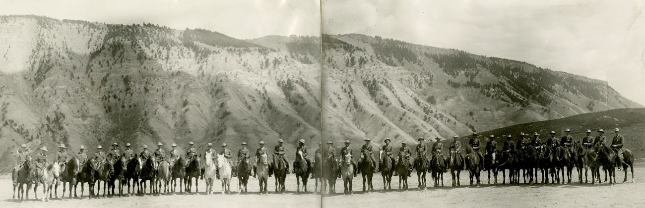 A line of Rangers on horseback are shown in a line with a mountain range behind them.