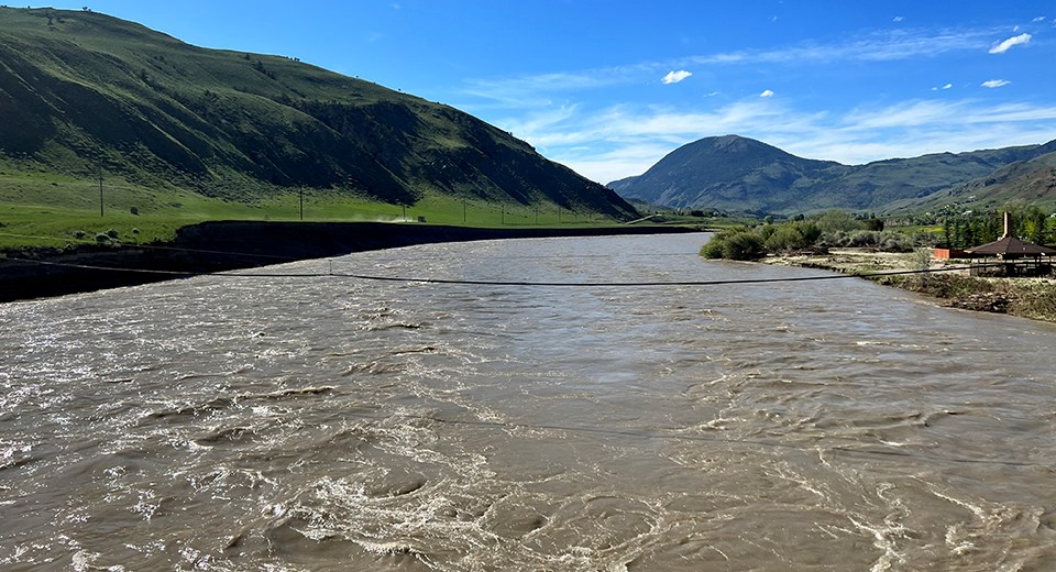 A turbulent, muddy river flowing between green hills.