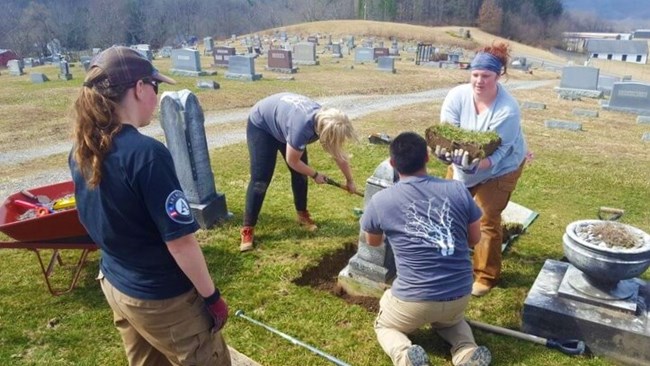 Four people perform conservation work, digging out a tract of land in a cemetery