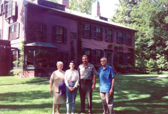 Four people stand on large grassy area in front of large home