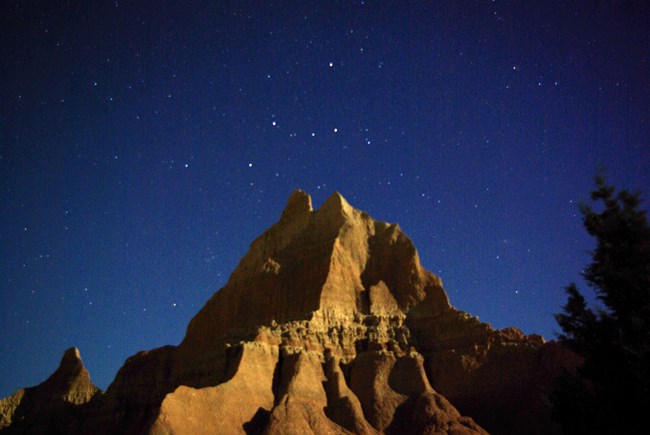 a single triangular badlands butte stretches up into a dark starry sky