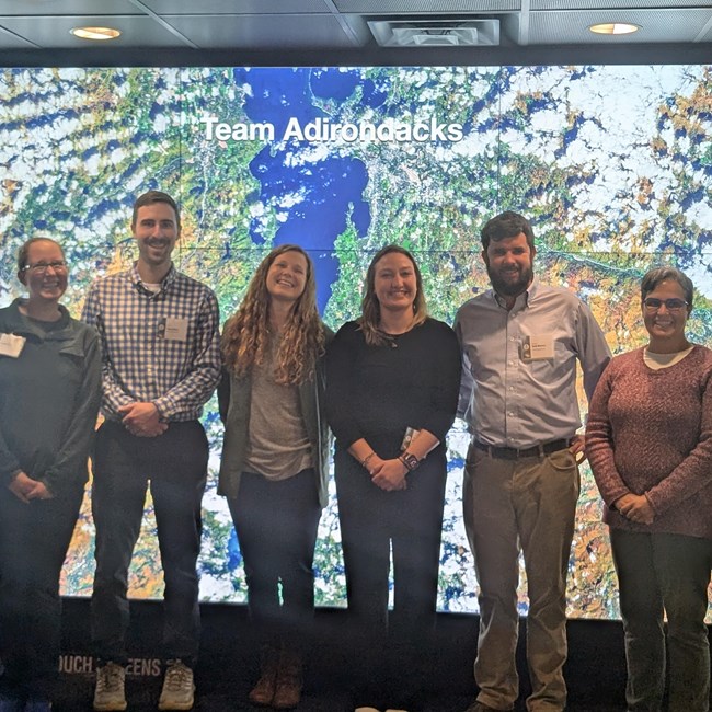 Six people stand in front of an arial map of earth