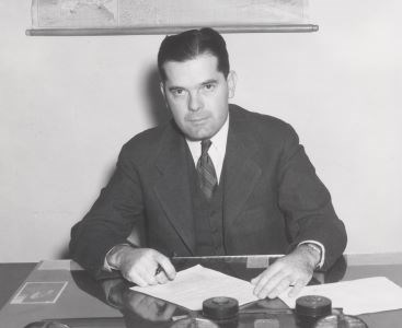 Aubrey Neasham in a suit sitting as his desk