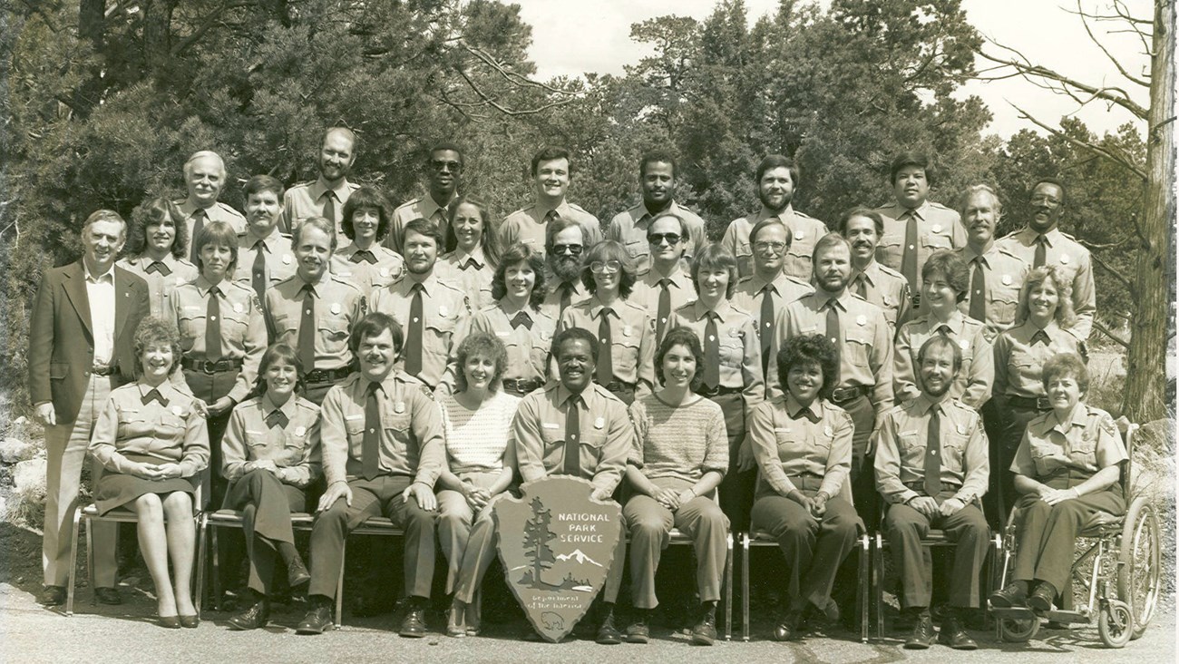 NPS employees pose for a group photo. Most wear NPS uniforms but a few are in street clothes. Shirley Beccue in her wheelchair is in the front row.