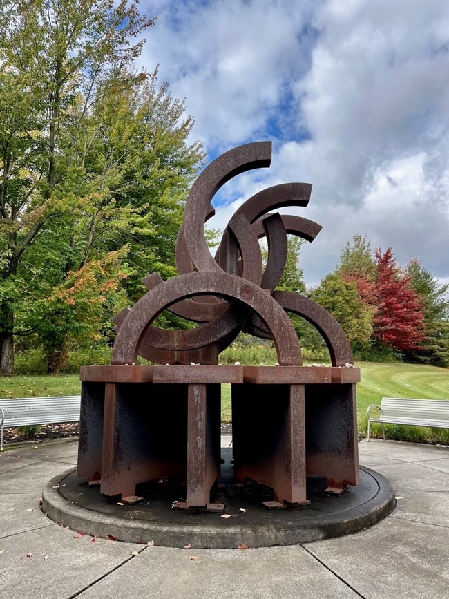 a rusted memorial of broken Olympic rings surrounded by gardens
