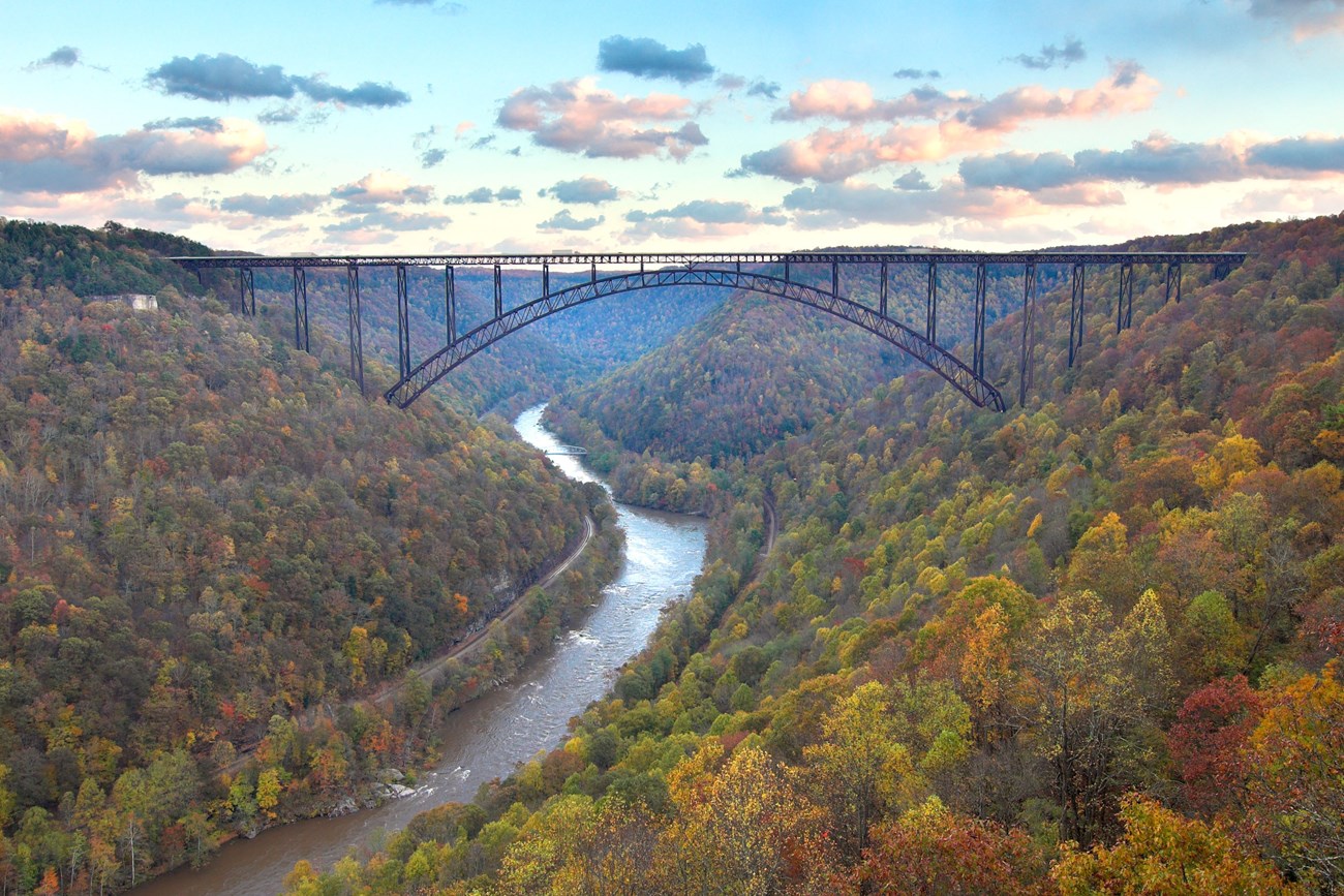 An aerial view of a river running through two hills filled with colorful trees and a bridge connecting them.