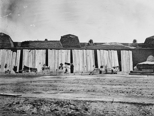 Black and white image of the interior of a fort with wooden boards leaning against the far side.