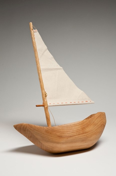 Miniature sailboat made out of wood, with a cloth flag